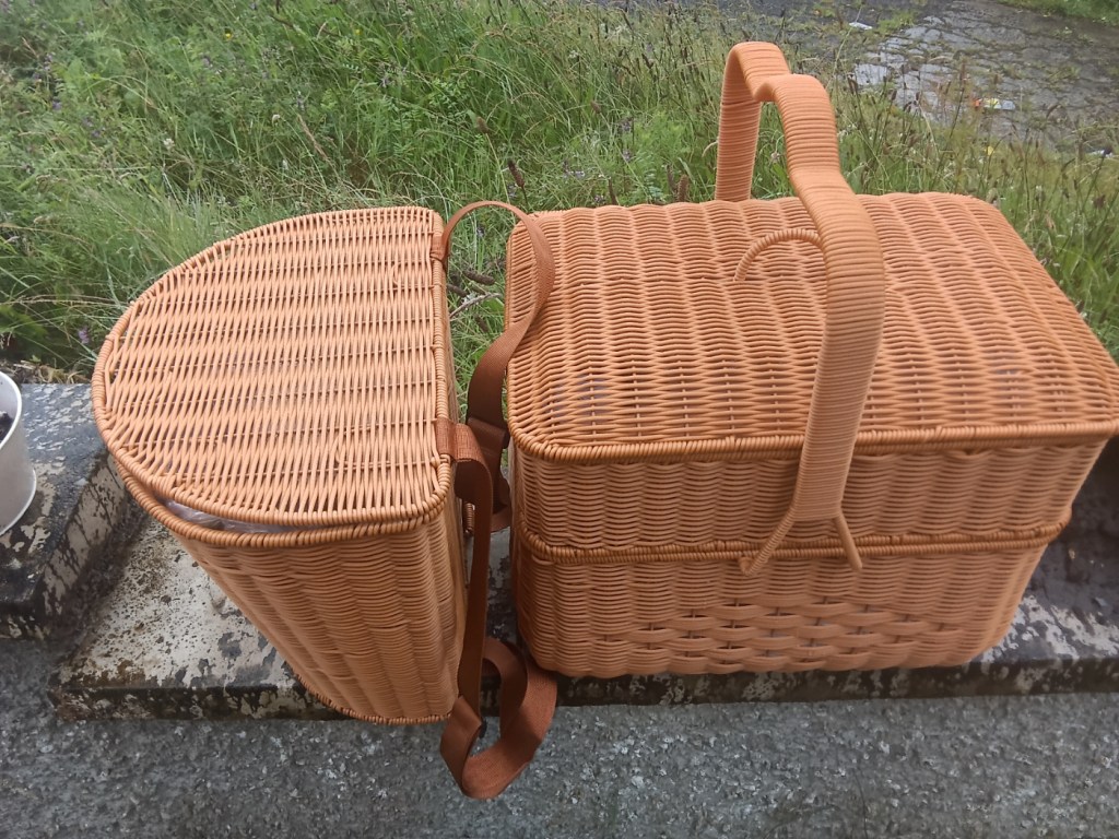 Image of 2 baskets: one a large 2-layer picnic basket containing the fibre I intend to spin this Tour de Fleece; the other smaller backpack-style basket is extra stash in case I get through the big basket. 